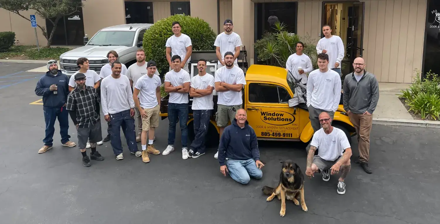 Team photo of My Window Solutions staff posing outside their office with a branded yellow truck and their company dog